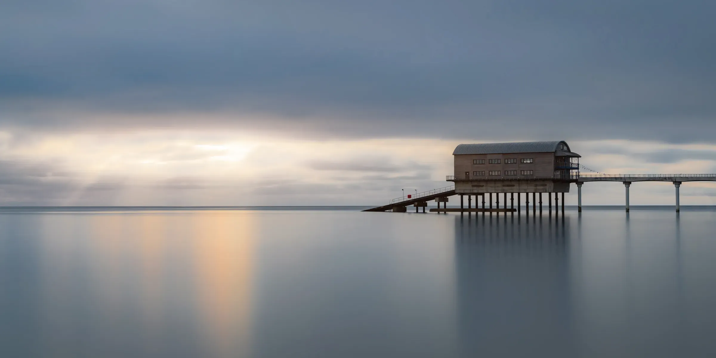 Bembridge Pier extending into a calm, long-exposure sea under soft grey skies, with minimal detail and a smooth reflective surface.