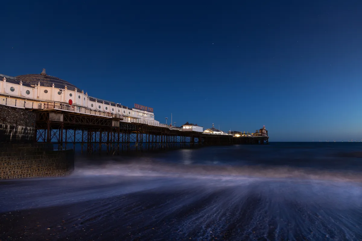 Brighton Palace Pier at blue hour with waves washing ashore beneath a deep twilight sky and cool coastal tones.