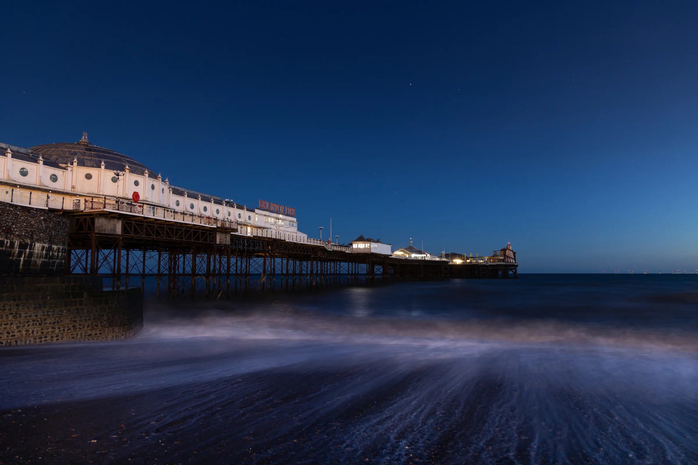 Brighton Palace Pier at blue hour with waves washing ashore beneath a deep twilight sky and cool coastal tones.