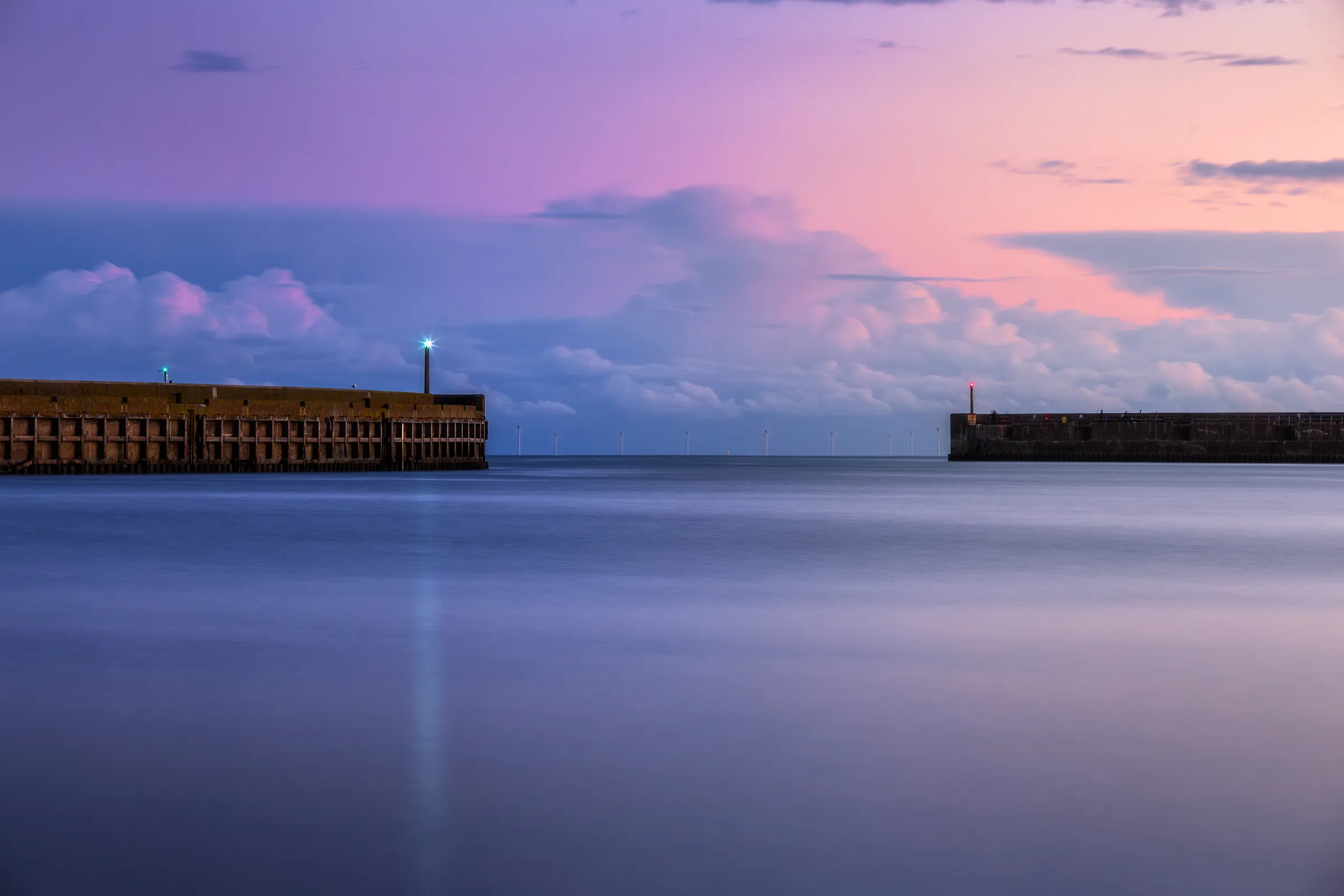 Two harbour walls frame a calm sea at dusk in Shoreham, with pastel pink and blue sky reflected in smooth long-exposure water.
