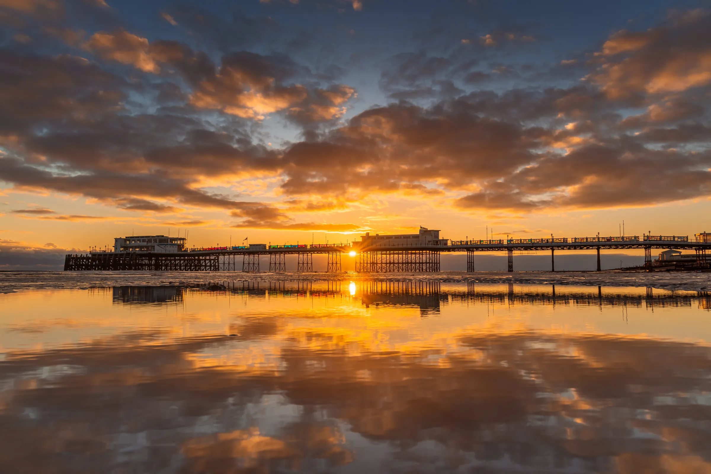 Worthing Pier at sunset with warm reflected light across wet sand and a glowing sky fading into evening.
