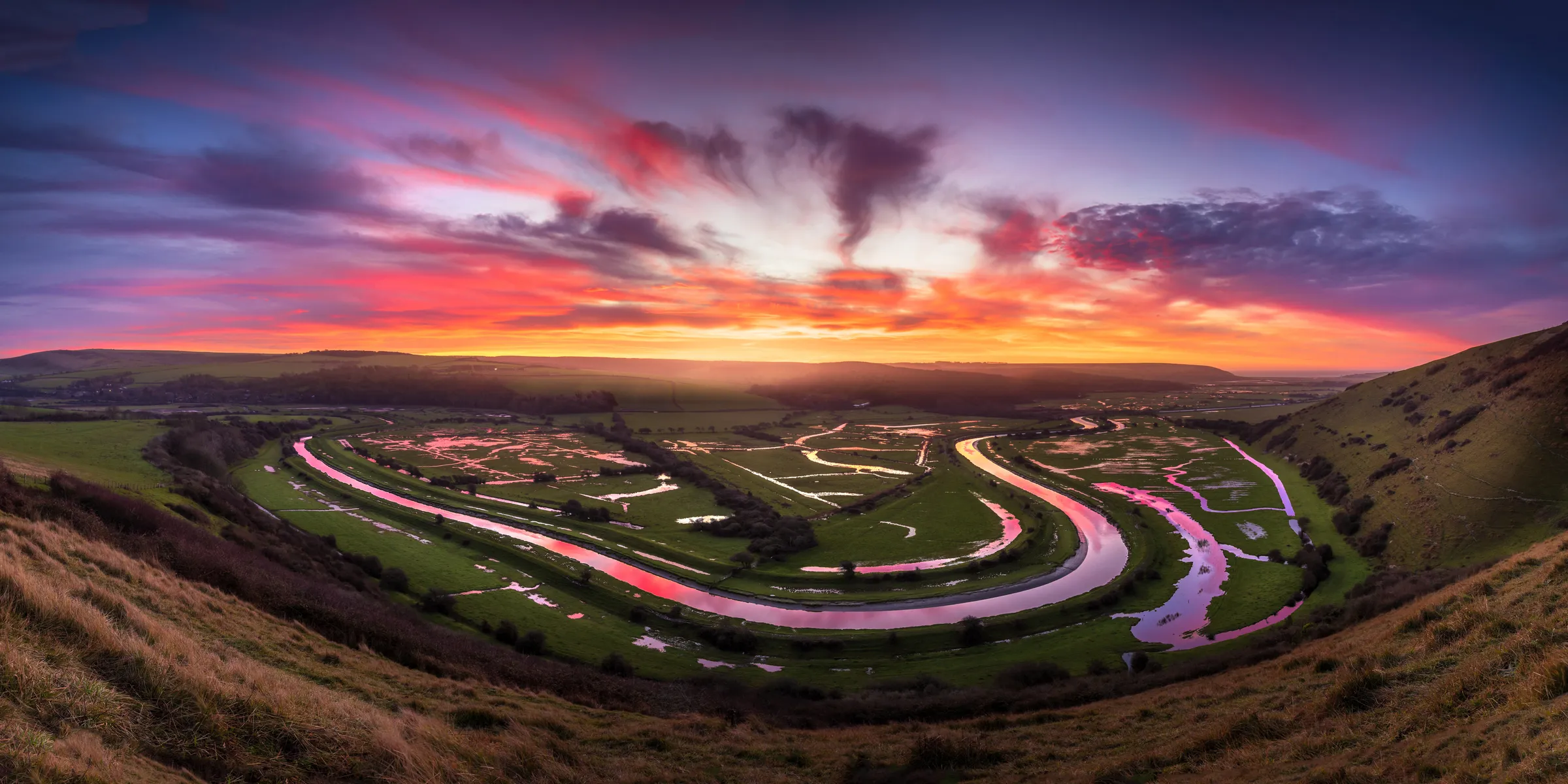 A sweeping sunrise over the Cuckmere meanders viewed from High and Over near Seaford, with vivid skies reflecting in the winding river.