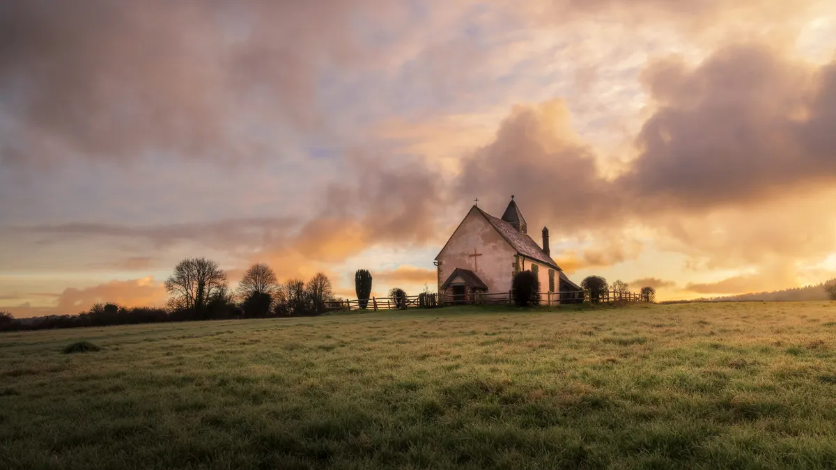 St Hubert's Chapel on a hill at sunrise in Idsworth, surrounded by open fields under warm glowing skies.