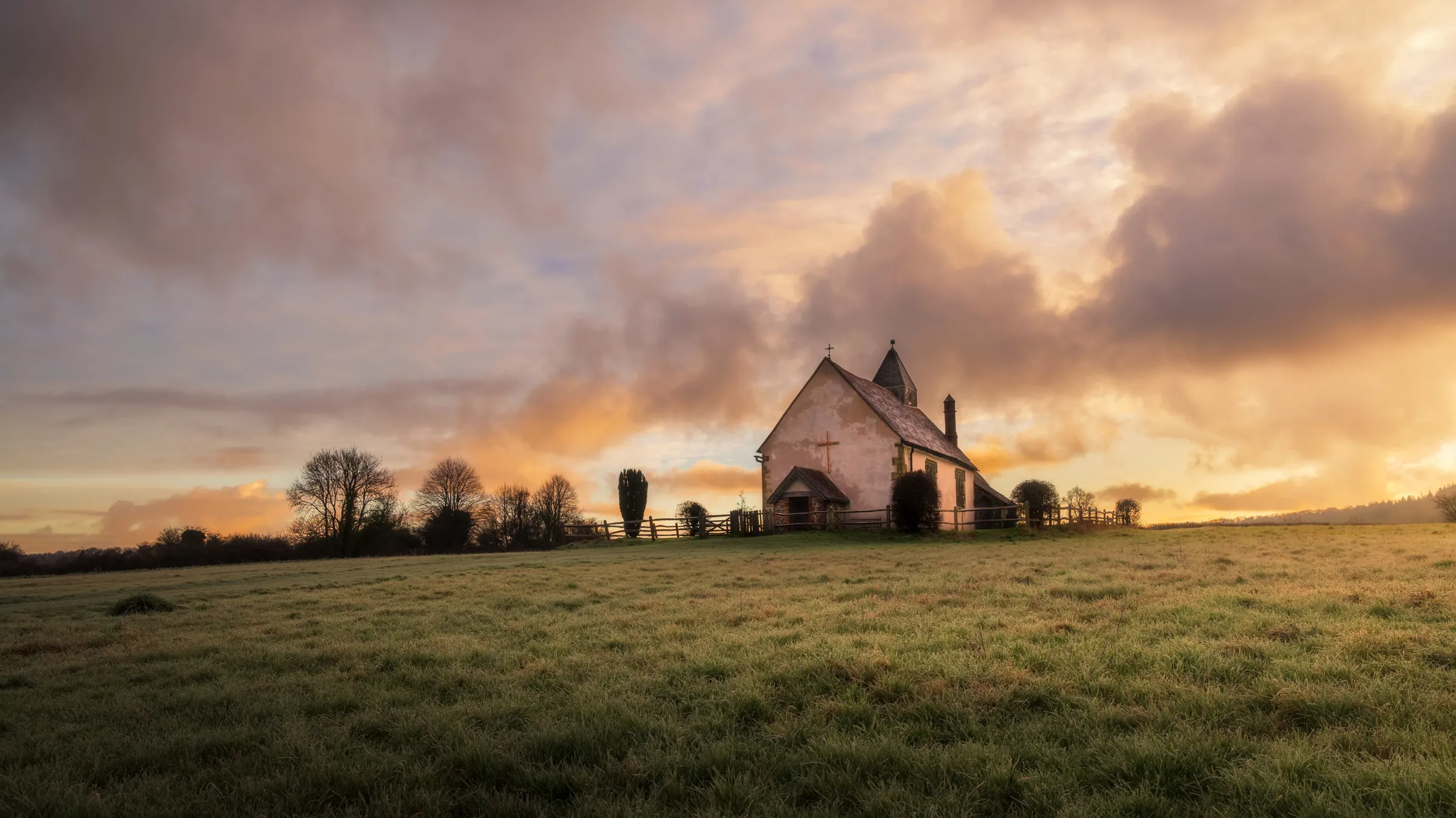 St Hubert's Chapel on a hill at sunrise in Idsworth, surrounded by open fields under warm glowing skies.