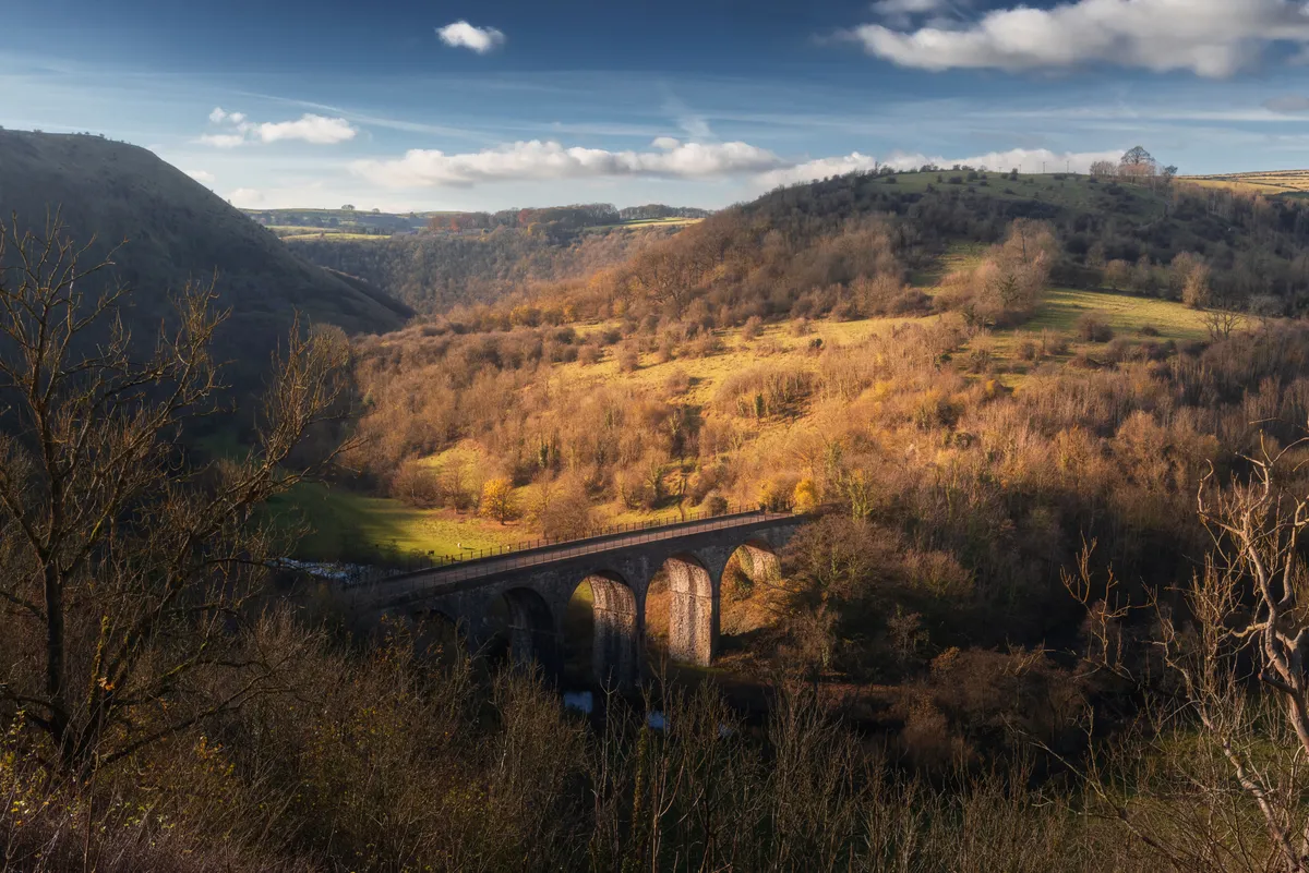 Monsal Head Viaduct crossing a valley in the Peak District, lit by low autumn sunlight with rolling hills beyond.