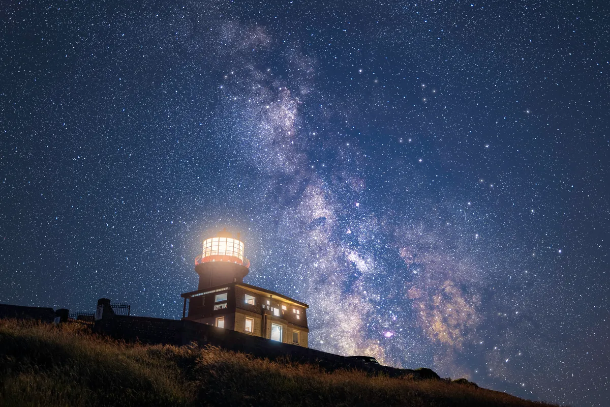 Belle Tout Lighthouse illuminated beneath the Milky Way, with a dense star field stretching across the night sky above Beachy Head.