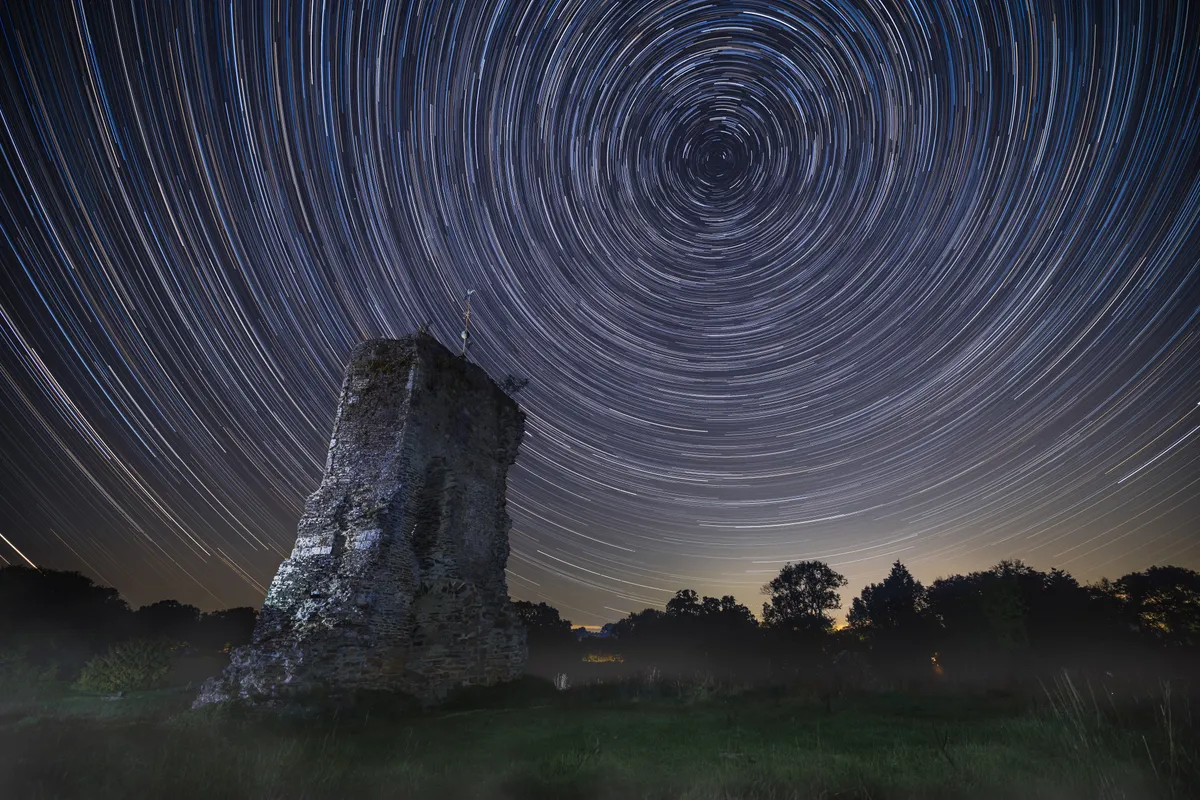 Ruins of Knepp Castle beneath tight circular star trails, with concentric arcs radiating around the celestial pole above the structure.
