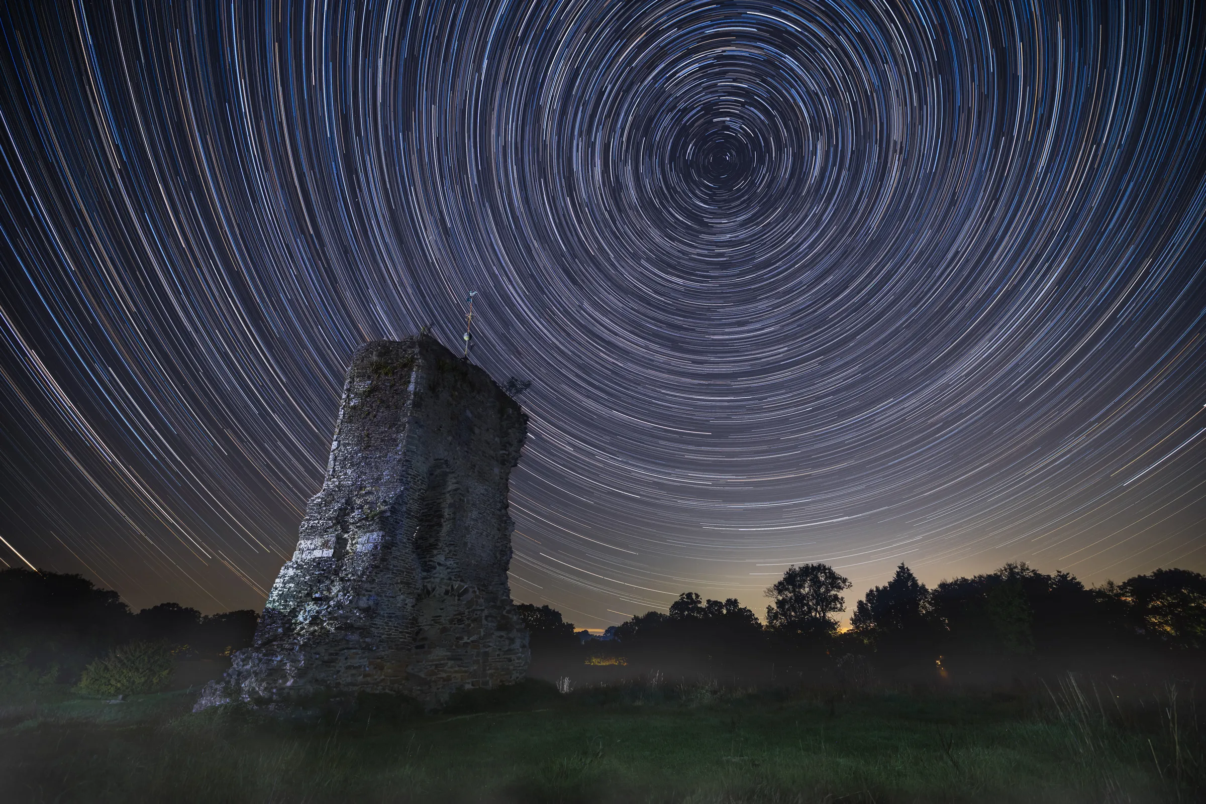 Ruins of Knepp Castle beneath tight circular star trails, with concentric arcs radiating around the celestial pole above the structure.