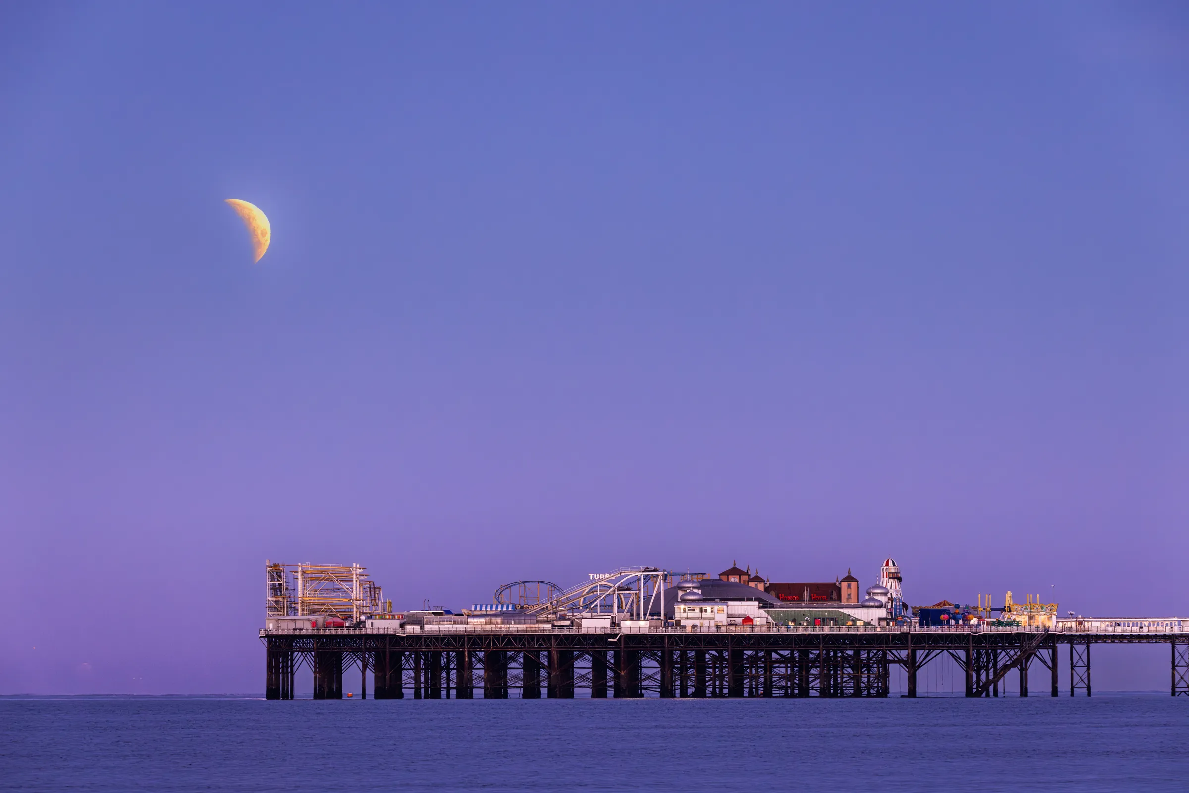 Brighton Palace Pier beneath a twilight sky with a partially eclipsed moon visible above the horizon.
