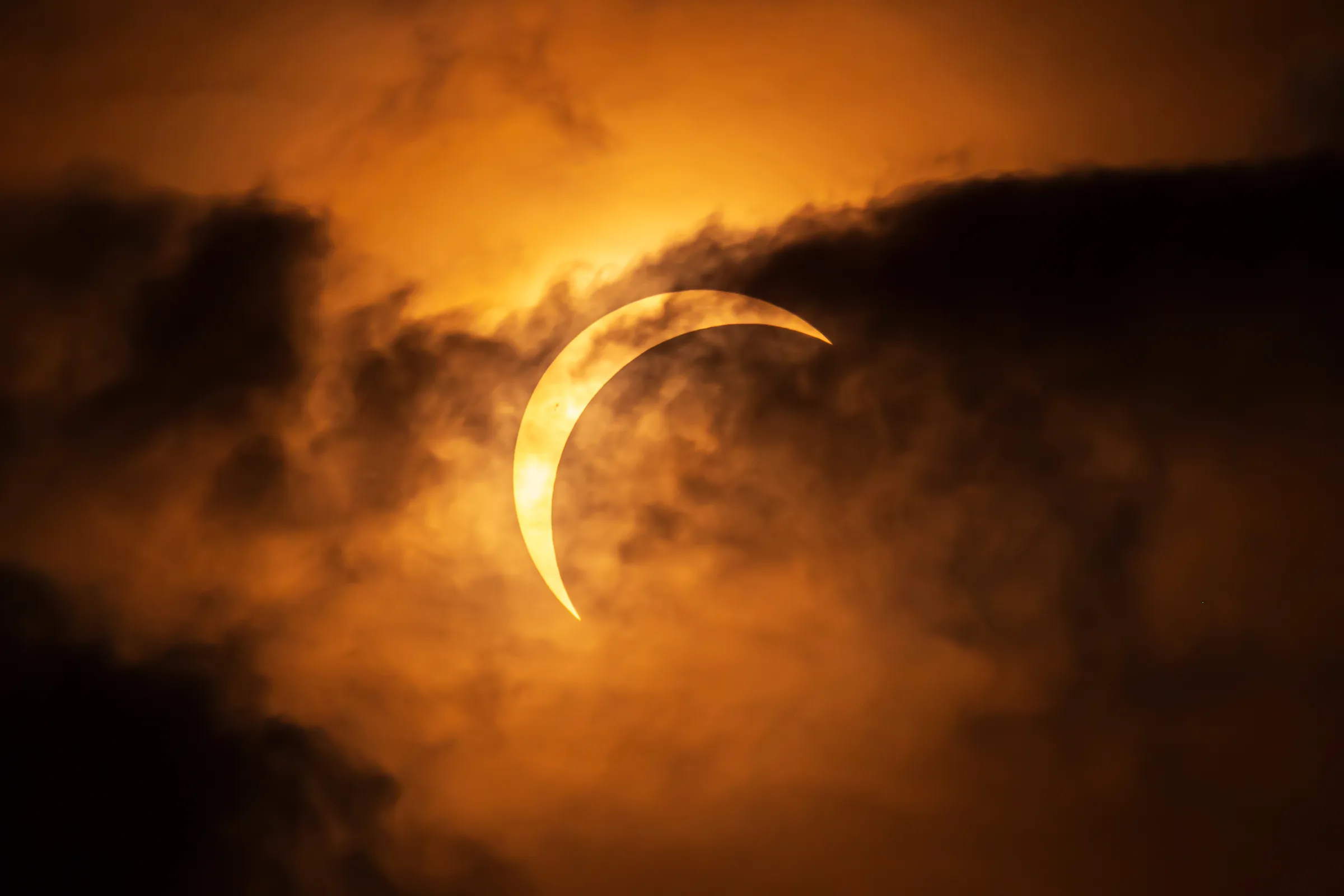 A crescent Sun during the August 2026 solar eclipse shining through dramatic layers of cloud above Talacre Beach in North Wales.