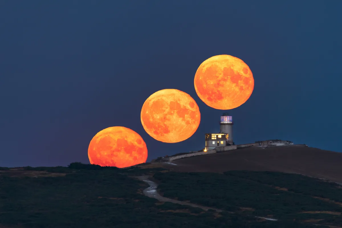 Sequence of the Sturgeon Moon rising behind Belle Tout Lighthouse at Beachy Head, with three positions of the moon aligned above the ridge.