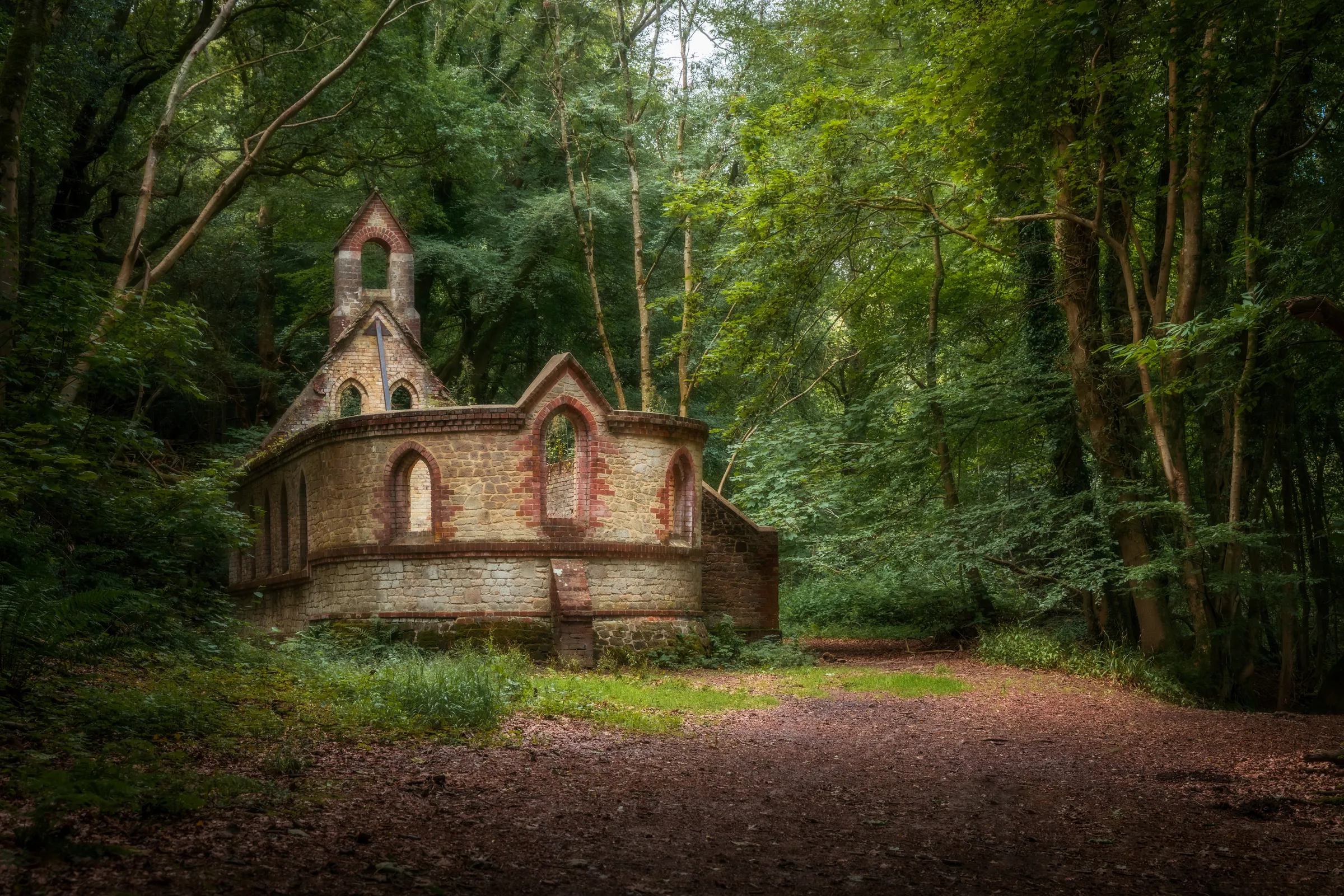 An old chapel ruin sits within dense woodland at Bedham, West Sussex, surrounded by trees and soft natural light.