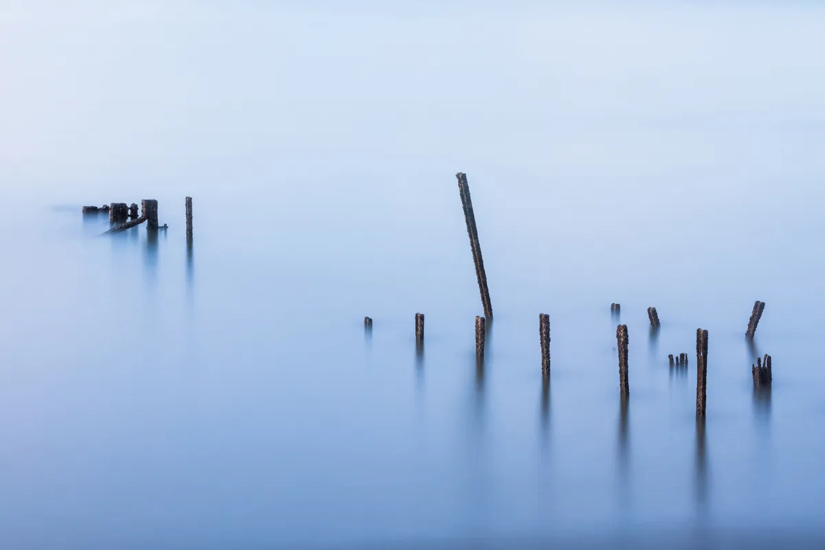 Weathered jetty posts emerging from calm long-exposure water at Newhaven
