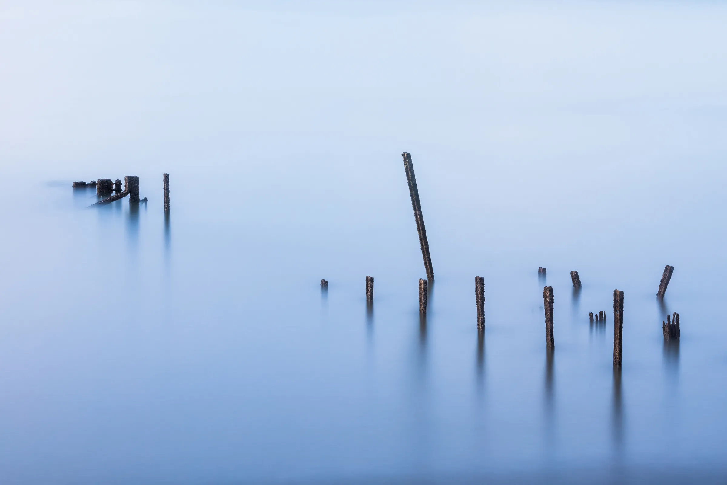 Weathered jetty posts emerging from calm long-exposure water at Newhaven in East Sussex