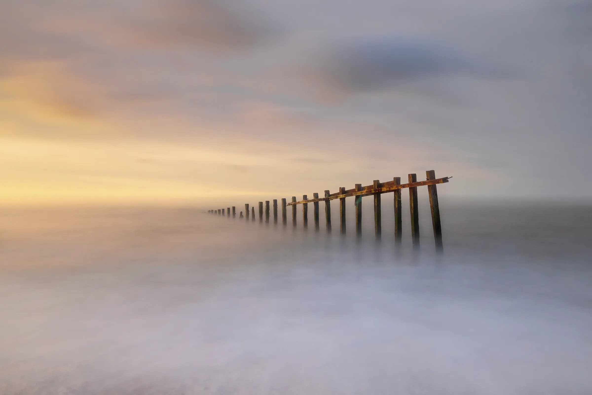 Old wooden groynes emerging from a misty long-exposure sea at Cuckmere Haven in East Sussex