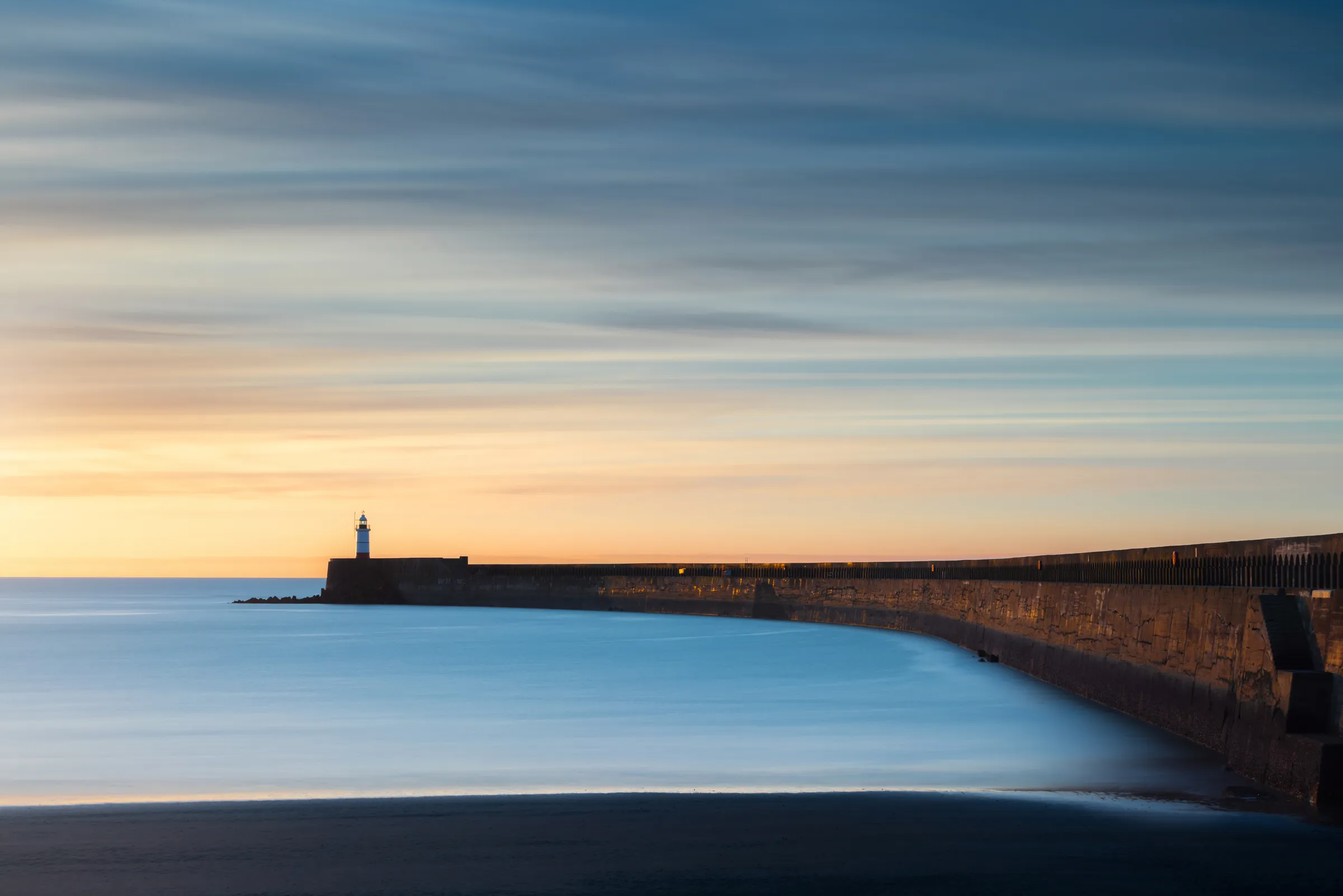 Newhaven harbour wall curving towards the lighthouse beneath streaked evening clouds