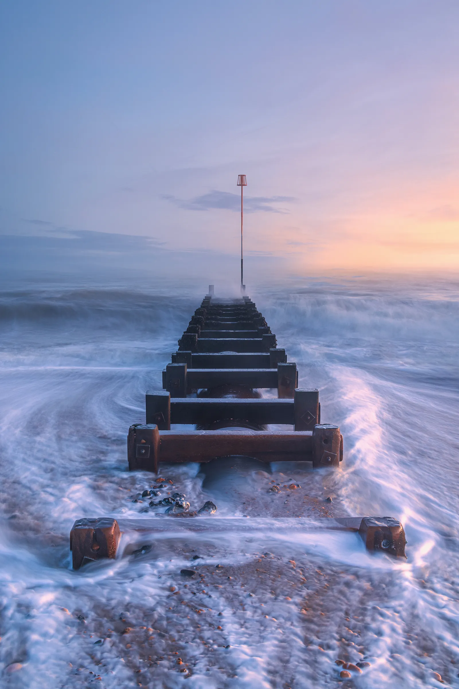A groyne at Worthing with seawater moving around it during soft coastal light